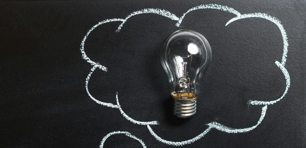 Light bulb laying on chalkboard with drawn thought bubble, symbolizing creative ideas.